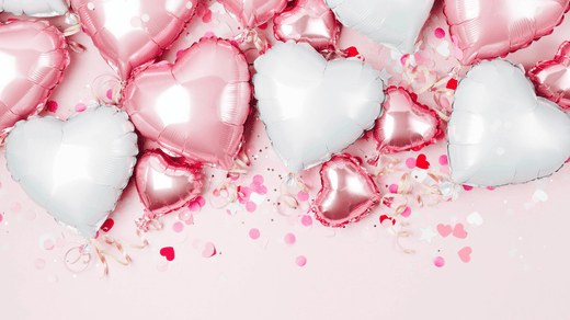 Heart-shaped balloons in shades of white and pink, surrounded by delicate red confetti, creating a romantic and festive decoration.