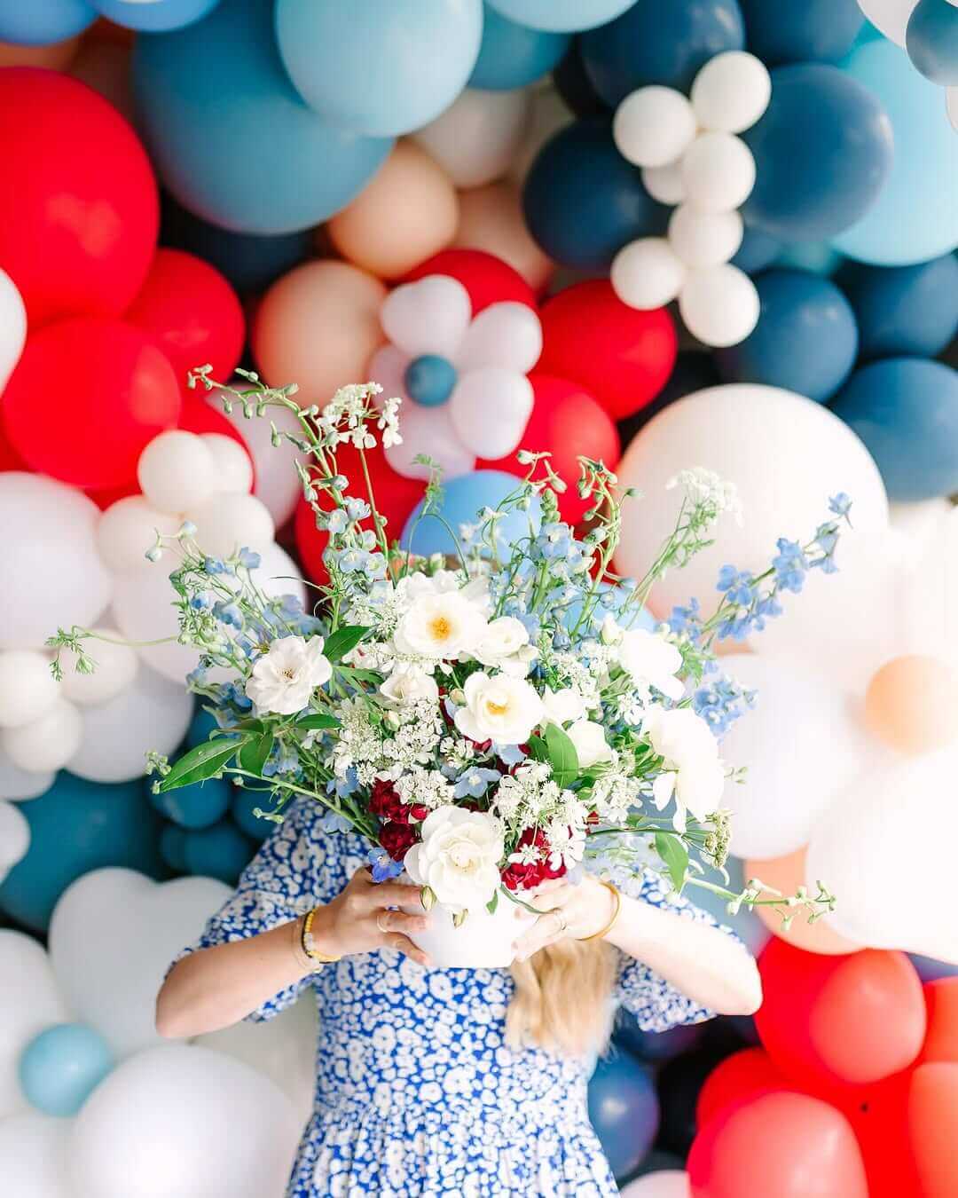 Luxury red, white, and blue balloon backdrop with a woman holding a floral bouquet. Perfect for event decor, birthday parties, and celebrations. Premium balloon decorations for elegant party styling.