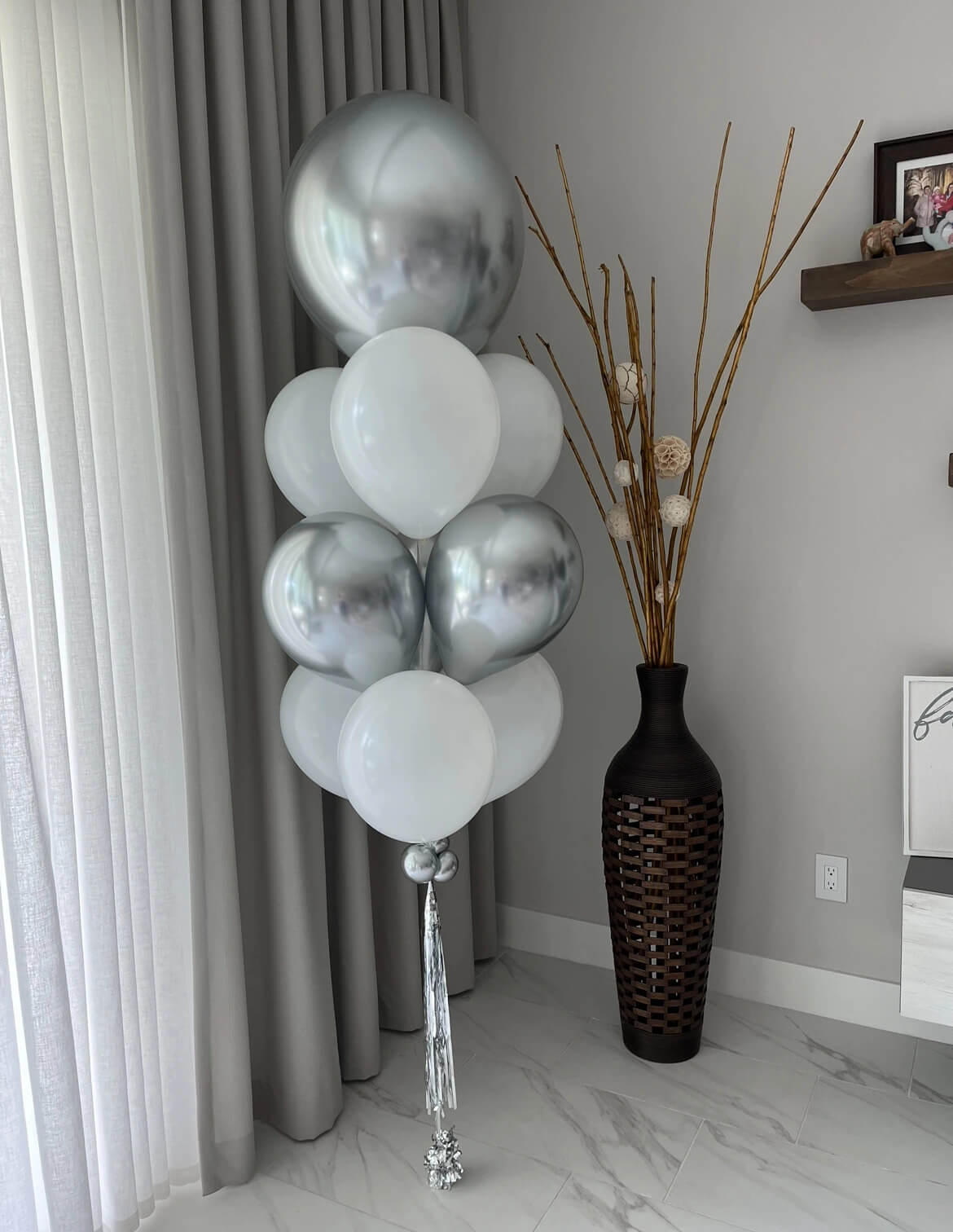 Elegant silver and white balloon arrangement with a silver tassel in a modern interior.