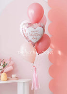 Valentine's Day balloon bouquet with a pink heart-shaped foil balloon reading "Happy Valentine's Day" and pink and blush latex balloons, tied with a pink tassel ribbon.