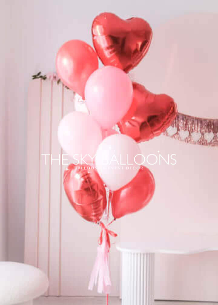 Valentine's Day balloon bouquet with red heart-shaped foil balloons and pink and white latex balloons, tied with pink tassel ribbons.